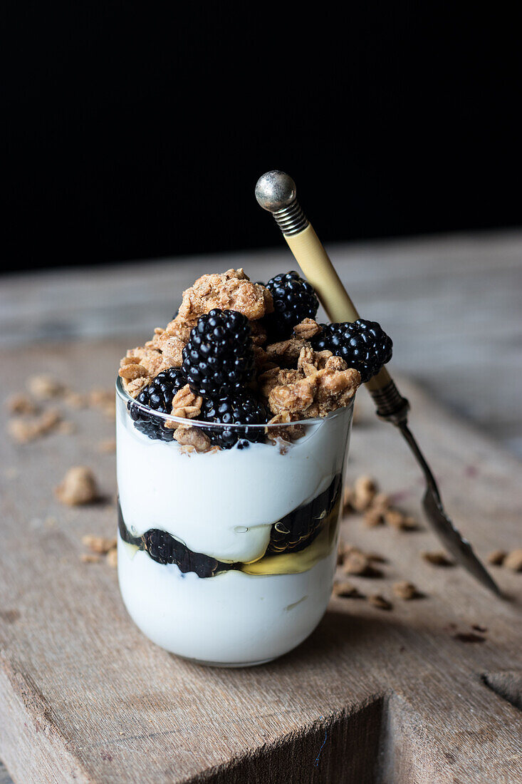 Closeup from above view of glass with walnut granola mixed with blueberries and yogurt placed on wooden chopping board near jar