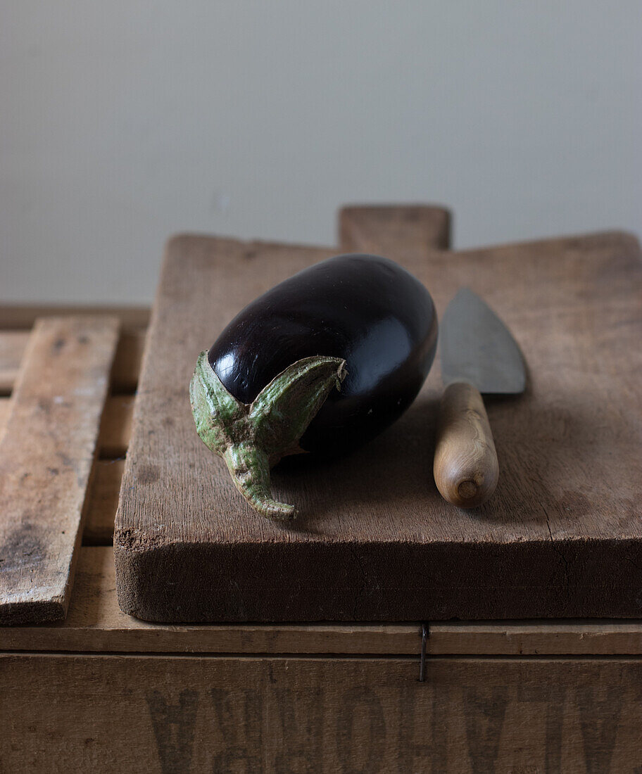 Frische reife Auberginen mit Messer auf einem Holzbrett auf einer Kiste