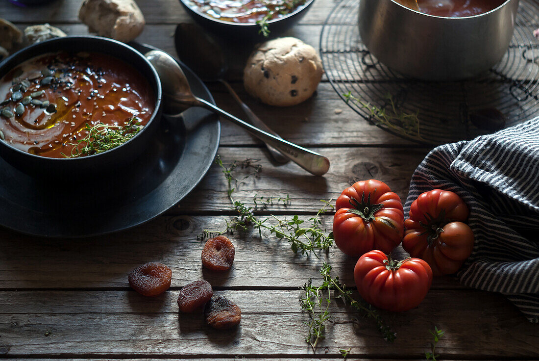 Komposition aus servierten Schalen mit köstlicher Tomatencremesuppe mit Kernen auf einem Tisch mit Tomaten und Brotbrötchen