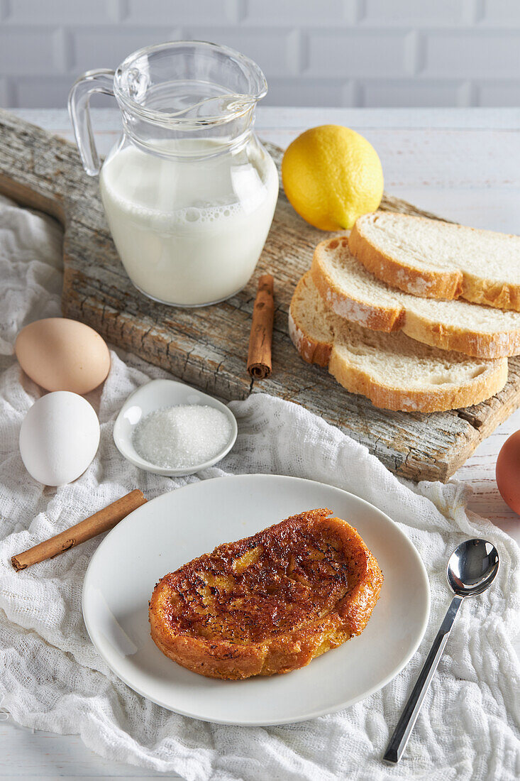 From above plate of appetizing Spanish torrija bread placed on table with raw eggs and sugar near wooden cutting board with jug of fresh milk and bread slices