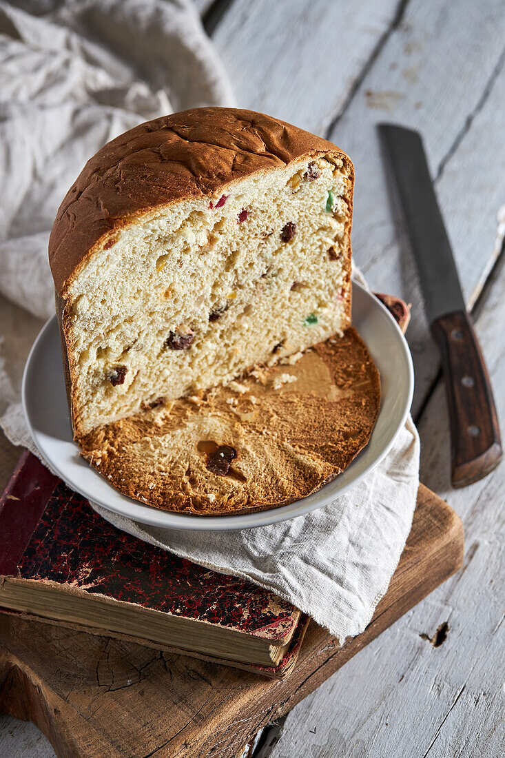 Stilleben mit frisch gebackenem, handwerklich hergestelltem Weihnachts-Panettone-Kuchen in Scheiben auf einem Buch und einem Schneidebrett vor dunklem Hintergrund