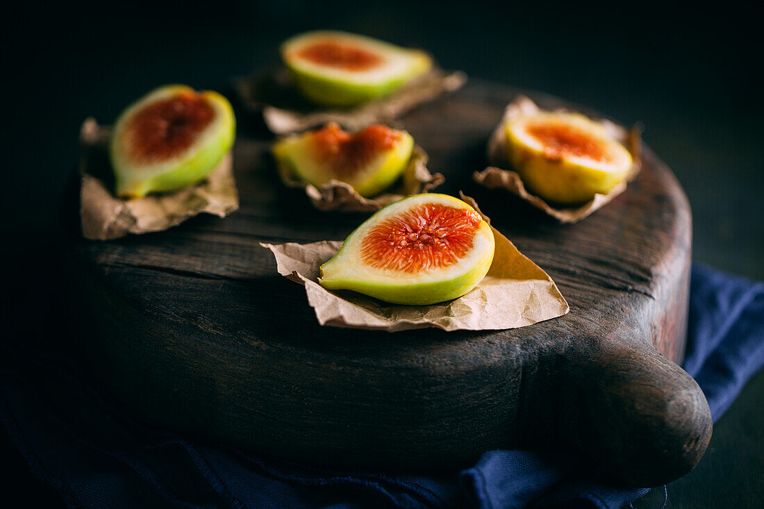 Fresh sweet figs arranged on wooden chopping board on dark background