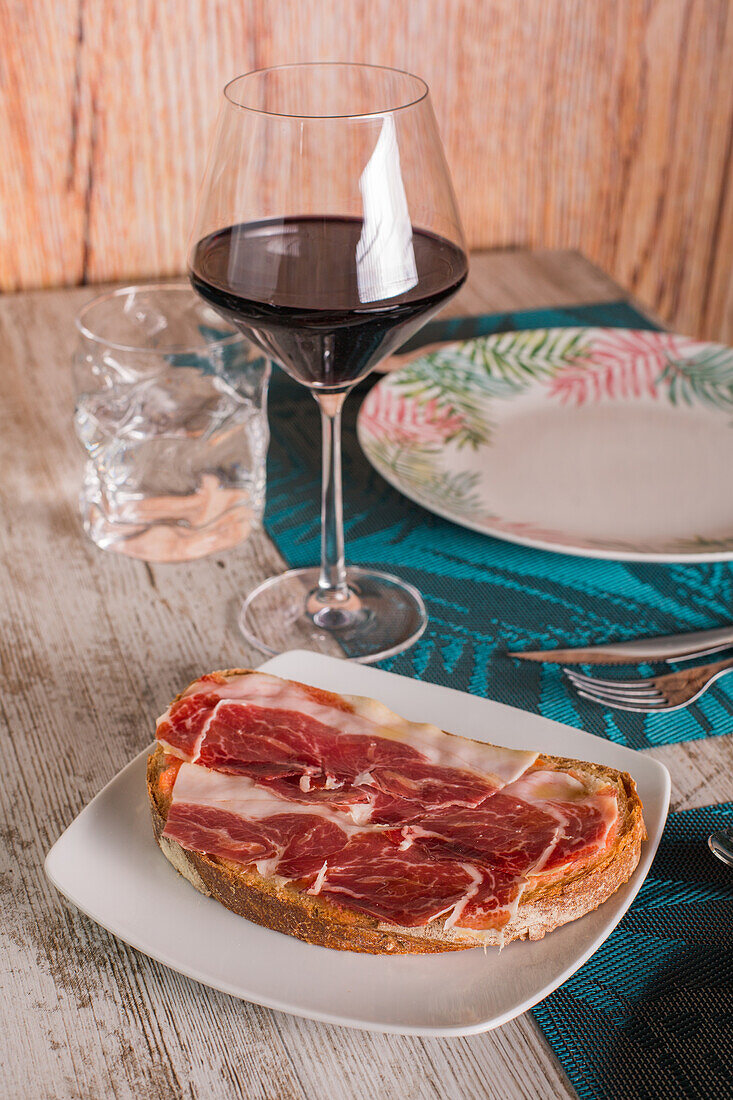Von oben köstliche Tapas mit Schinken serviert auf einem Teller auf dem Tisch mit einem Glas Rotwein im Restaurant