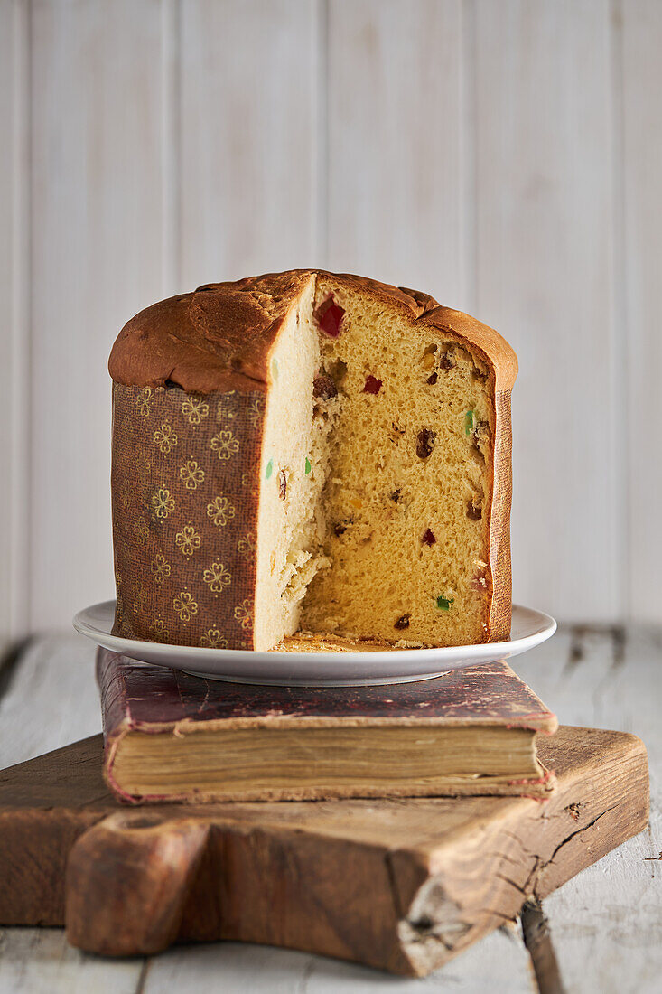 Still life of sliced fresh baked artisan Christmas panettone cake on vintage book and cutting board against light background