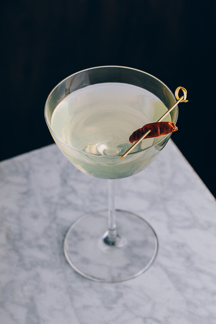 From above glass goblet of martini cocktail garnished with red pepper served on table against black background