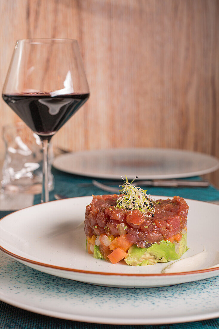 Gourmet red tuna tartare with sauce on plate served with glass of red wine on table in restaurant