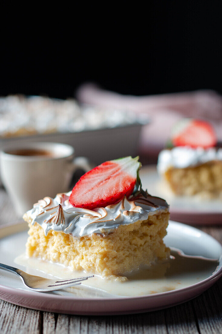 Sweet delicious piece of three milks cake with half fresh strawberry on white plate on wooden table