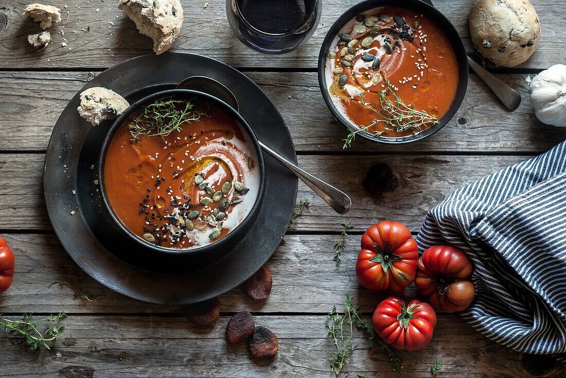 Flache Schalen mit cremiger Tomatensuppe, garniert mit Kernen und serviert auf einem Tisch mit Tomaten und getrockneten Aprikosen