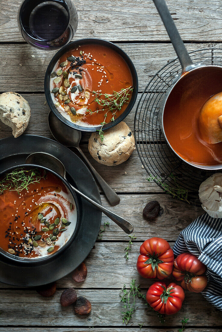 Flat lay of bowls with creamy tomato soup garnished with seeds and served on table with tomatoes and dried apricots