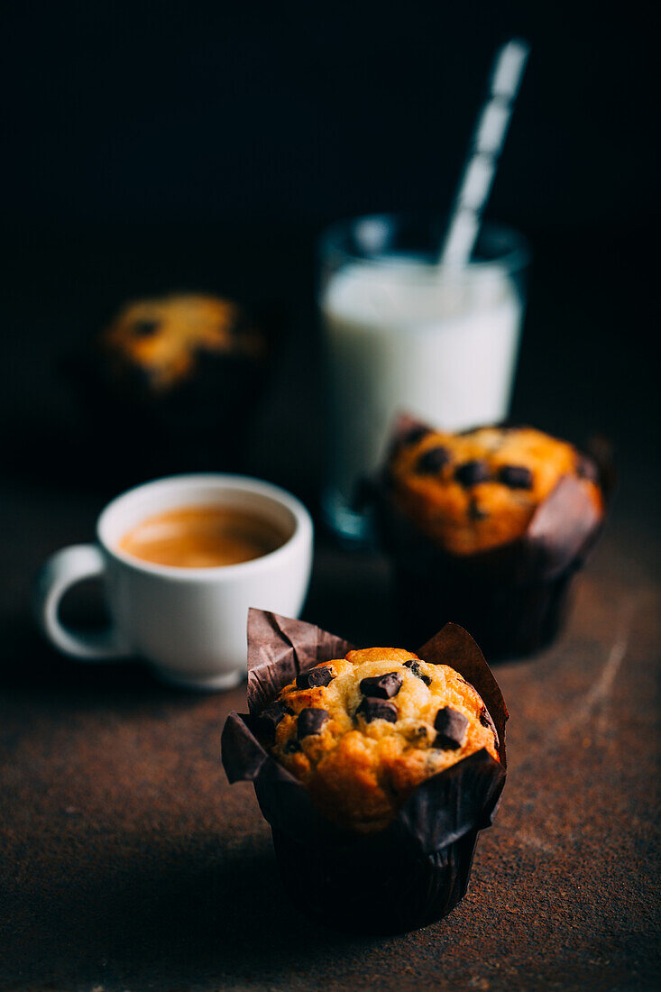 Chocolate muffins, milk and coffee cup on dark background