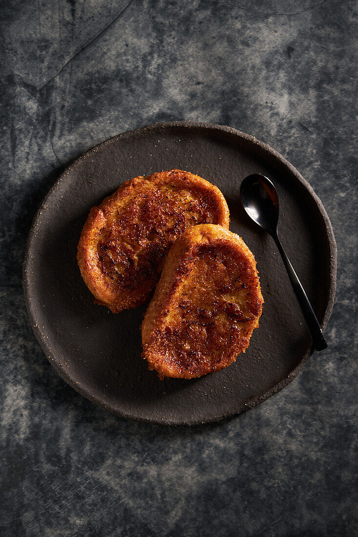 High angle of delicious homemade torrija with crunchy crust placed on black plate with spoon on marble table