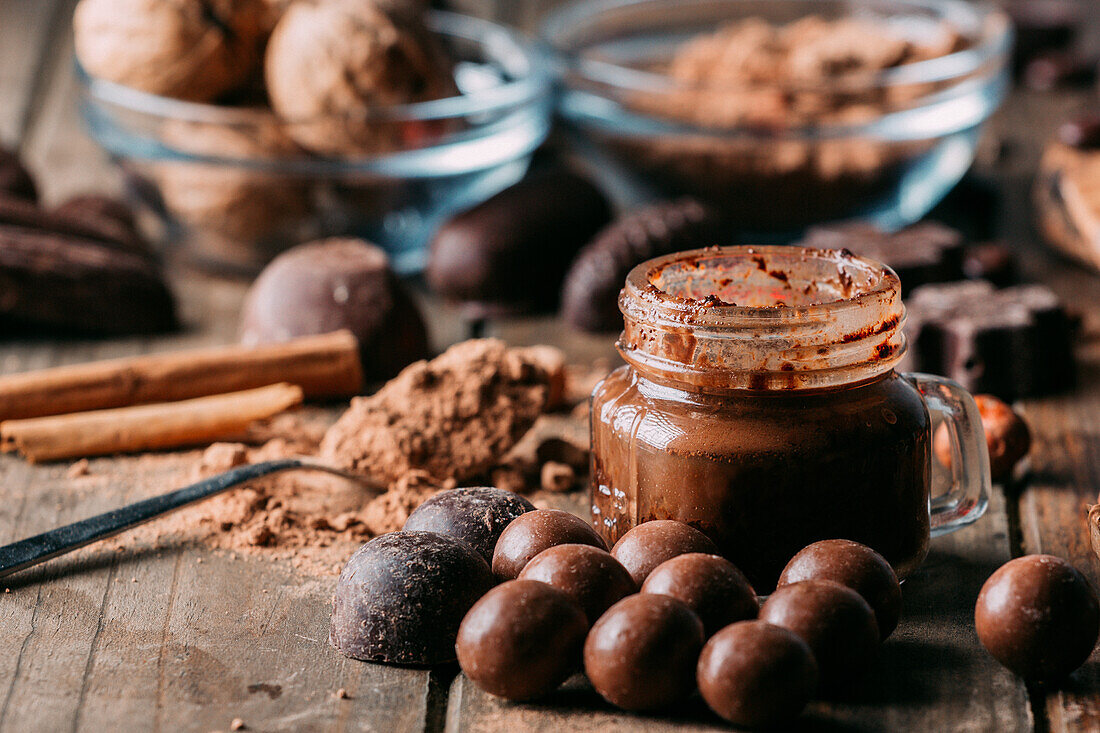 Verschiedene Schokoladenbonbons und ein Glas Mousse auf einem Holztisch mit einem Löffel mit Kakaopulver und Zimtstangen