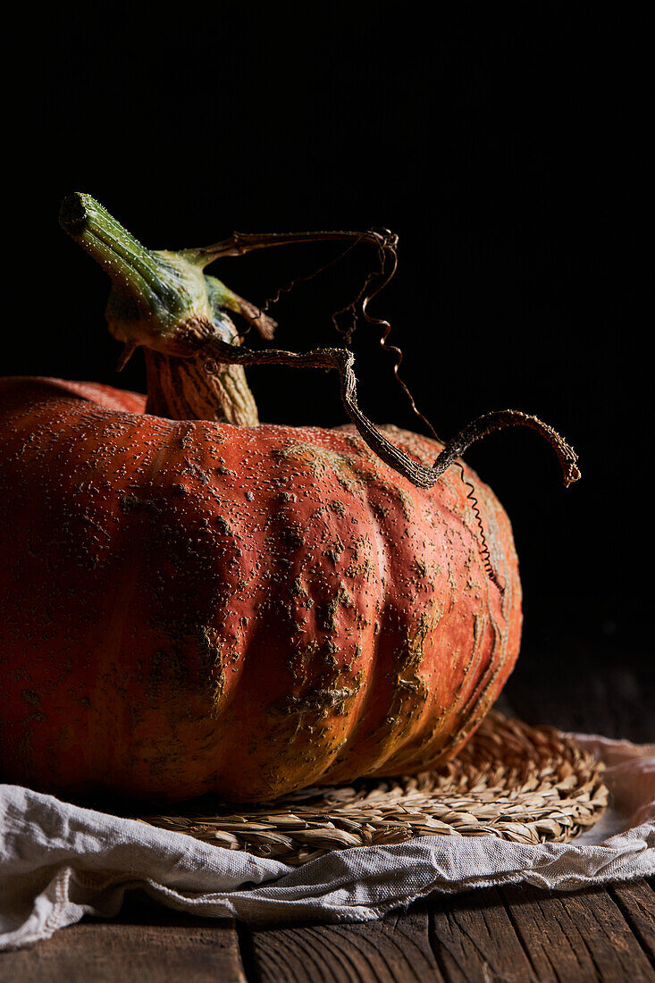 Whole ripe pumpkin with slightly ribbed skin placed on wooden table on placemat against black background