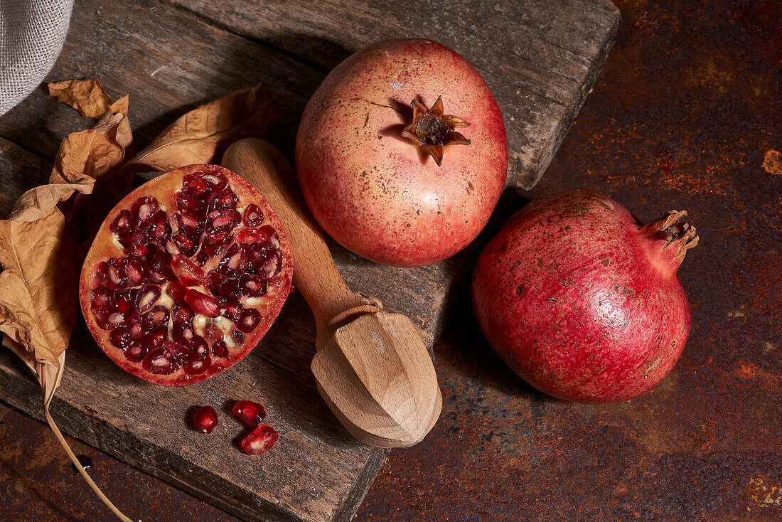 From above fresh whole pomegranate and seeds arranged on wooden board near squeezer