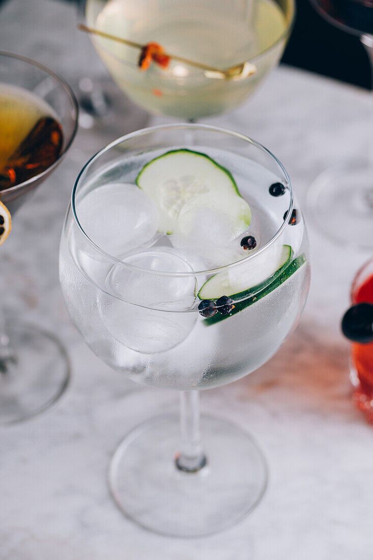 Glass of refreshing alcohol gin tonic cocktail with sliced cucumber and ice cubes on table