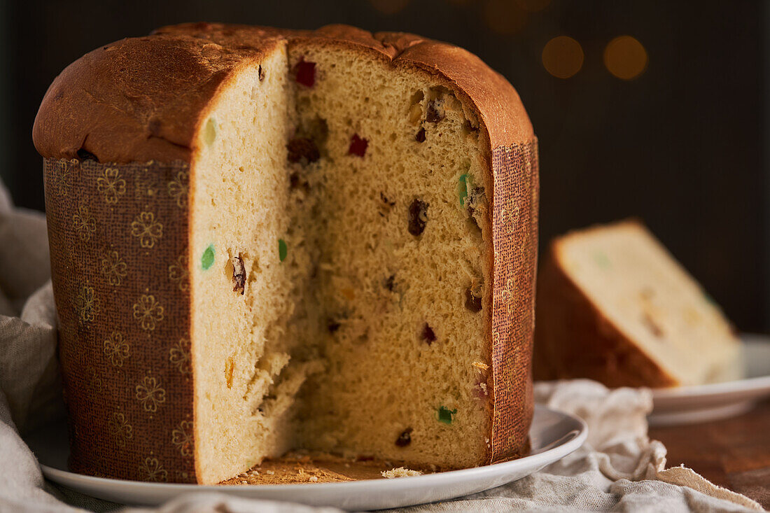 In Scheiben geschnittener, frisch gebackener, handwerklich hergestellter Weihnachts-Panettone-Kuchen unter warmem Licht vor Bokeh-Hintergrund