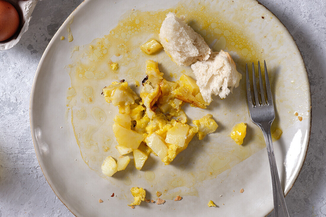 Draufsicht auf einen schmutzigen Teller mit Resten von spanischem Omelett und Brot auf einem Tisch in der Küche