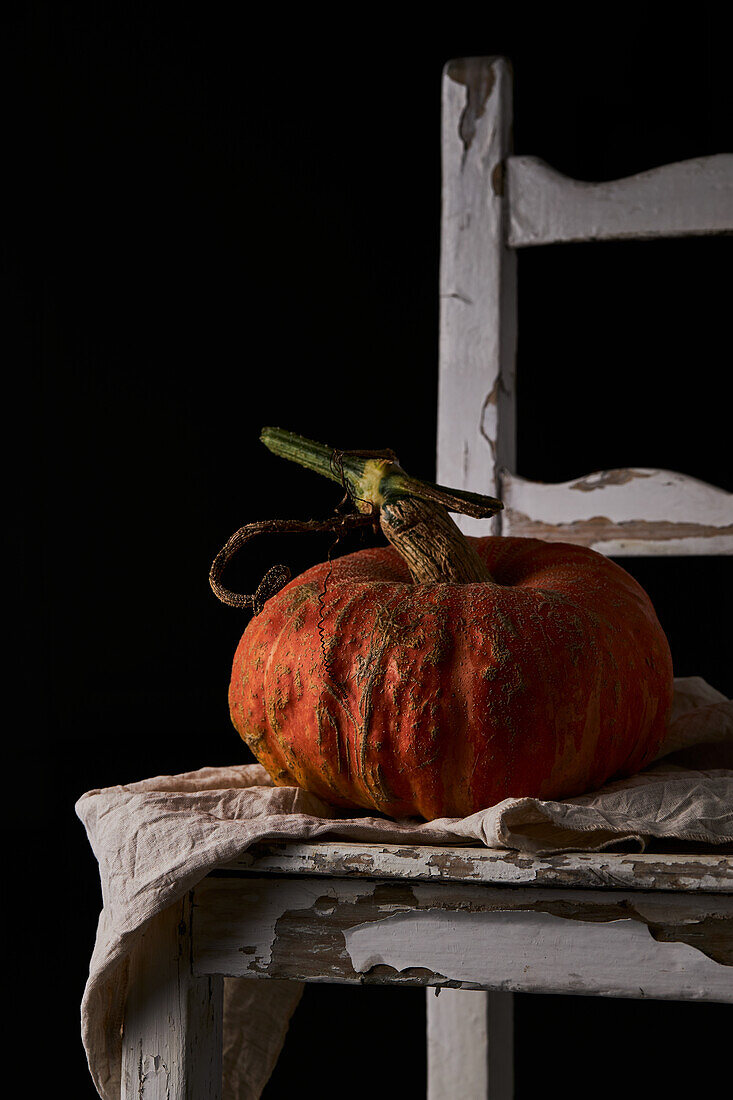 Whole ripe pumpkin with slightly ribbed skin placed on wooden white chair against black background