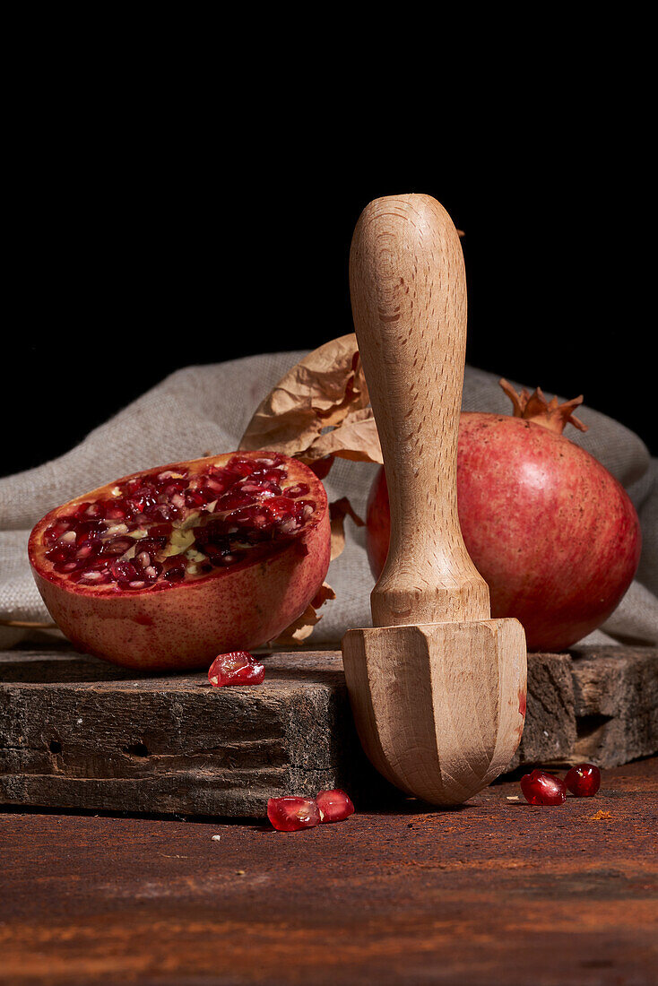 Fresh whole pomegranate and seeds arranged on wooden board near squeezer