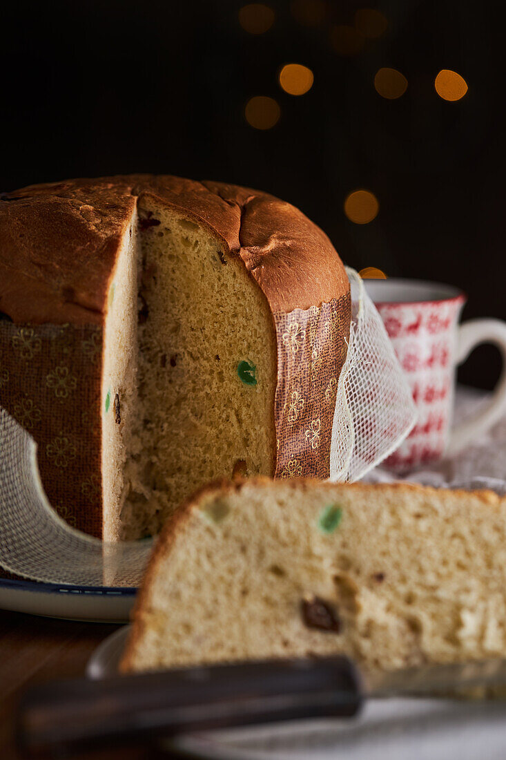 In Scheiben geschnittener, frisch gebackener, handwerklich hergestellter Weihnachts-Panettone-Kuchen unter warmem Licht vor Bokeh-Hintergrund