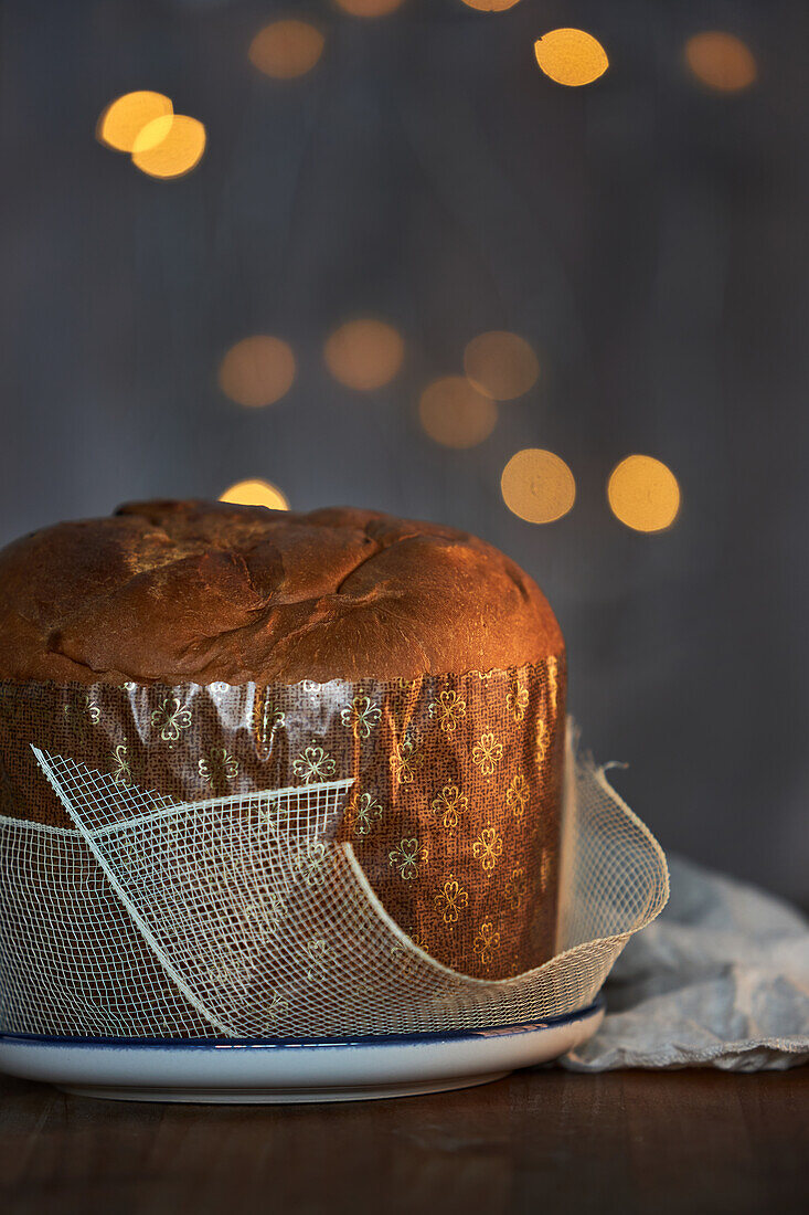 Ungeschnittener, frisch gebackener, handwerklich hergestellter Weihnachts-Panettone-Kuchen unter warmem Licht vor Bokeh-Hintergrund