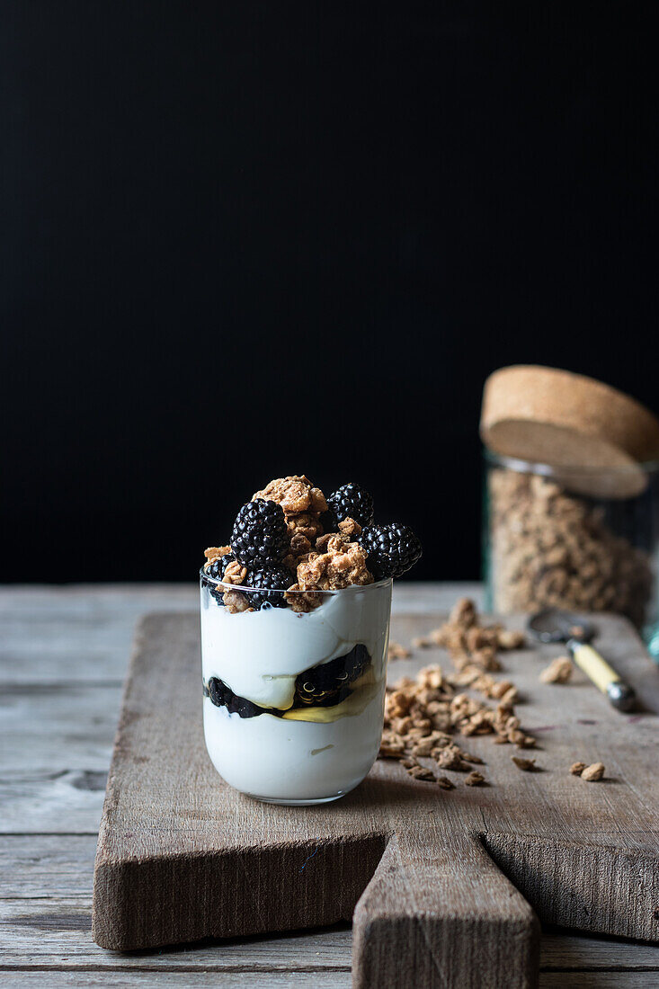 Closeup from above view of glass with walnut granola mixed with blueberries and yogurt placed on wooden chopping board near jar