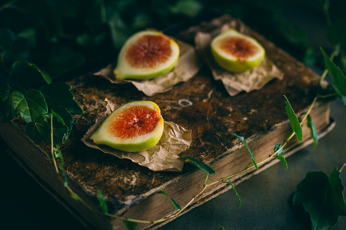 Fresh sweet figs arranged on wooden chopping board with green leaves