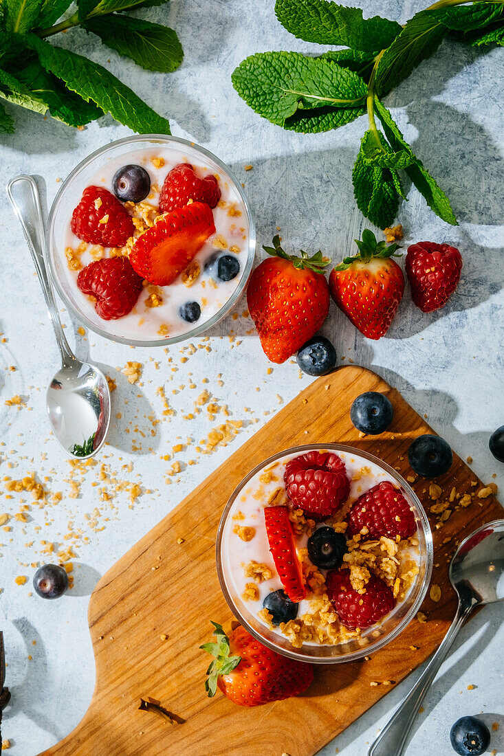 Blick von oben auf köstlichen hausgemachten Joghurt mit Erdbeeren, Beeren und Müsli auf weißem Hintergrund