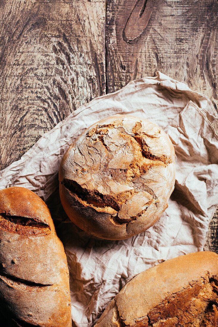 Draufsicht auf frisch gebackene leckere Sauerteigbrote in verschiedenen Formen auf einem Holztisch in einer Bäckerei