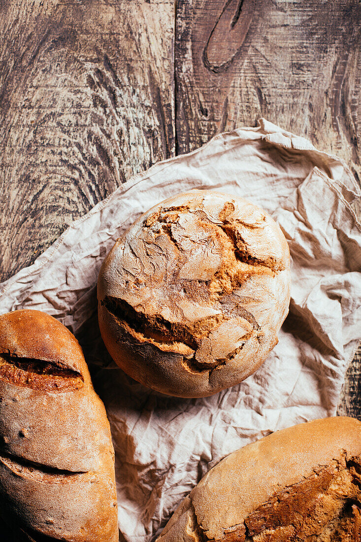 Top view of freshly baked delicious sourdough breads of various shapes placed on wooden table in bakery