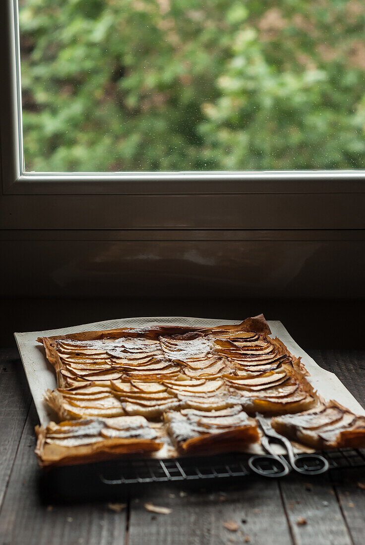 Delicious baked apple pie with frangipane cut into pieces and composed on cooling rack near window