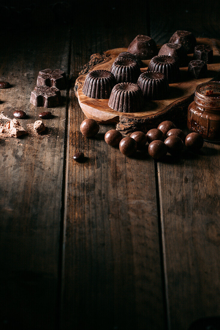 From above set of tasty handmade chocolates placed on wooden cutting board near mousse jar in kitchen