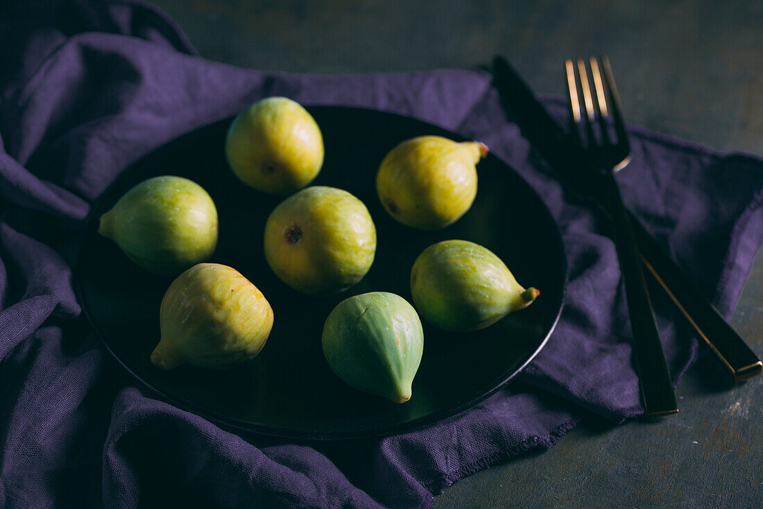 Top view of fresh sweet figs arranged on plate with fabric napkin on dark background