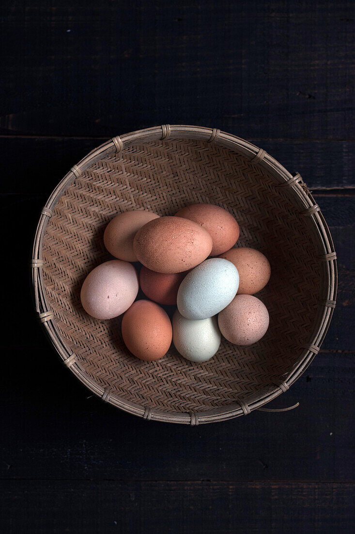 Blick von oben auf einen mit braunen und weißen Eiern gefüllten Weidenkorb auf einem Tisch