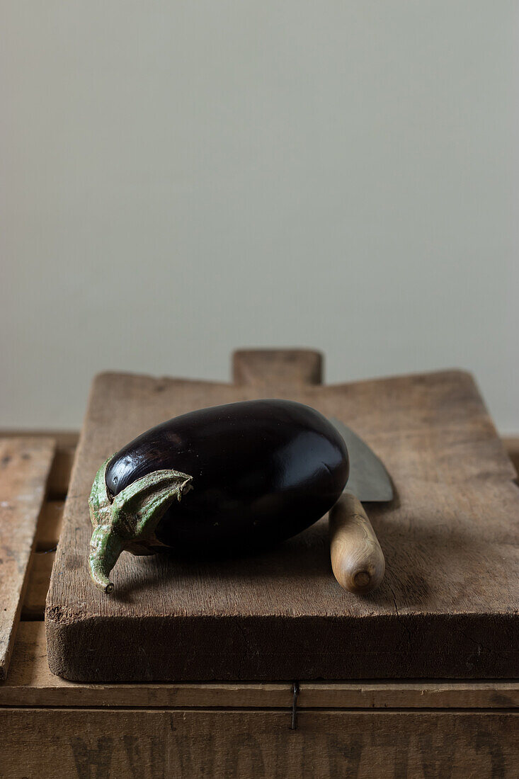 Fresh ripe eggplant with knife laid on wooden chopping board on box