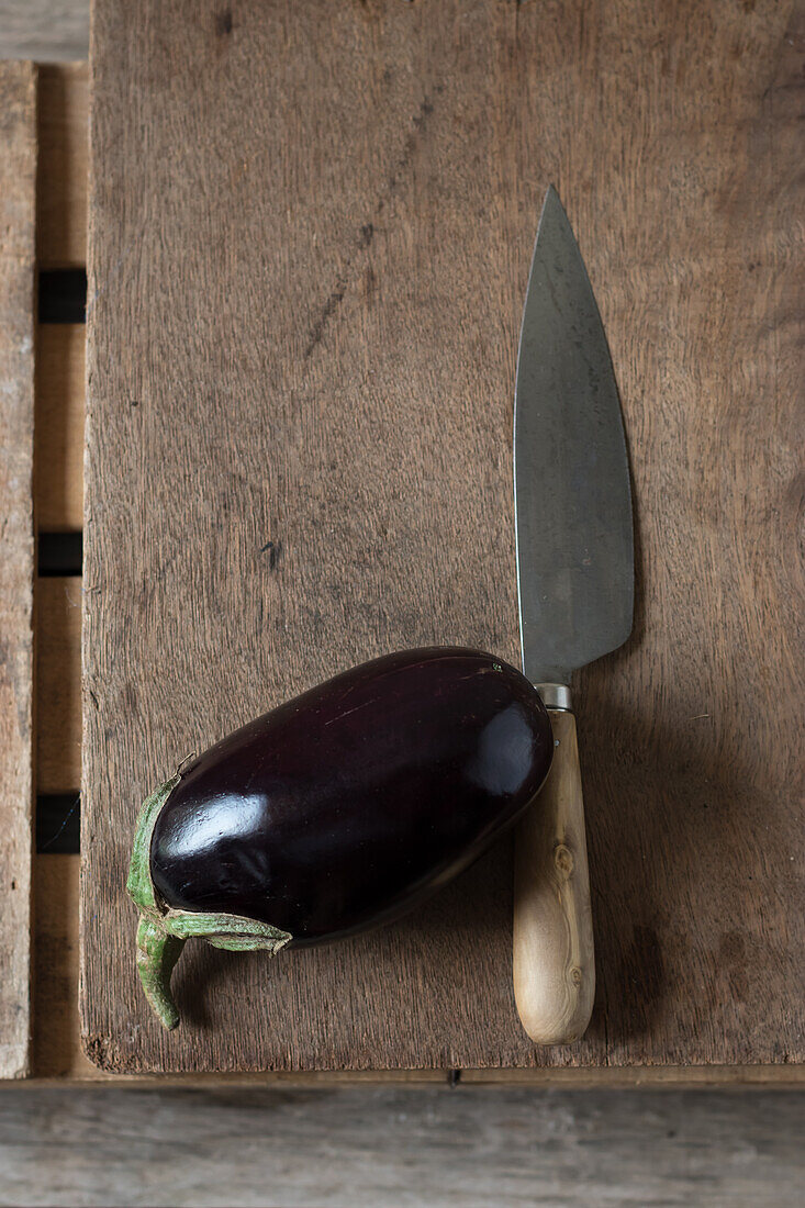 Fresh ripe eggplant with knife laid on wooden chopping board on box