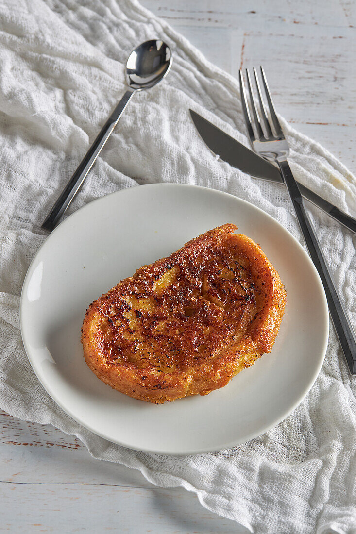 High angle of appetizing crispy torrija placed on plate and served on white wooden table with fork and knife