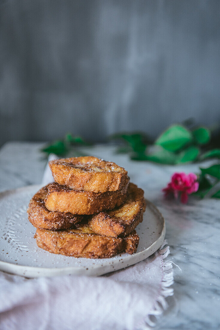 Hausgemachtes traditionelles spanisches Osterdessert mit französischem Toast, serviert auf einem Teller neben einer Rosenblüte auf marmoriertem Hintergrund