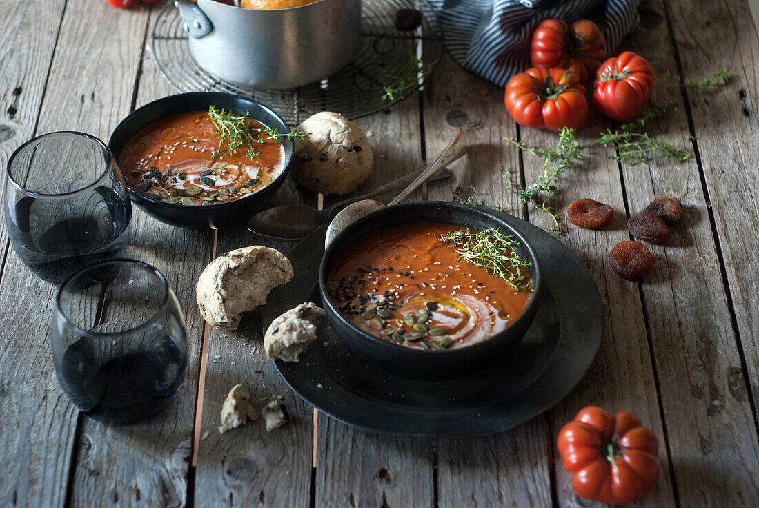 Komposition aus servierten Schalen mit köstlicher Tomatencremesuppe mit Kernen auf einem Tisch mit Tomaten und Brotbrötchen