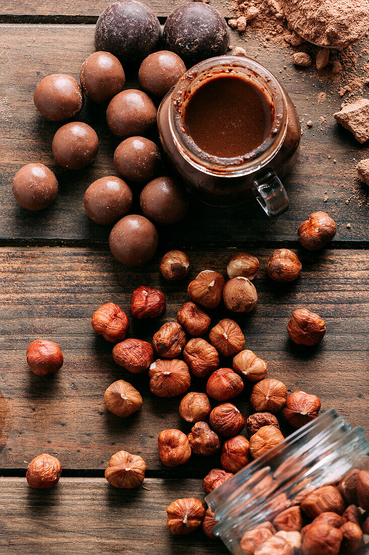 Top view of various handmade chocolates with nuts arranged on wooden table with peanut butter and cinnamon sticks