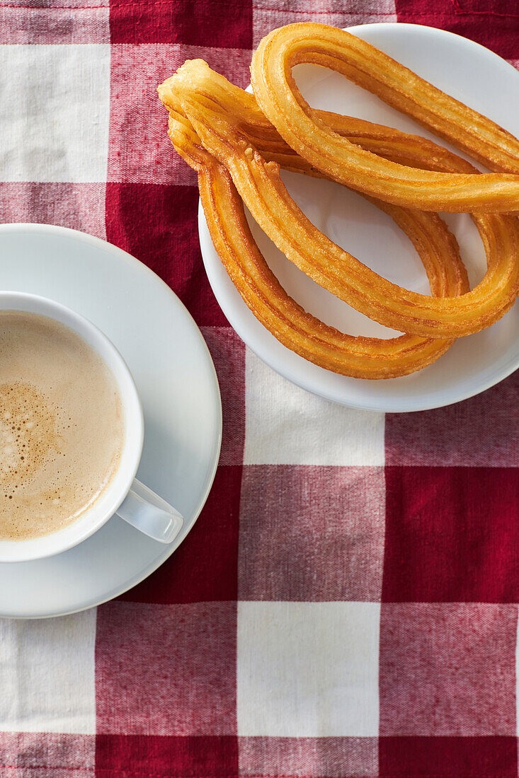 Appetizing churros on plate and cup of fresh morning coffee served on napkin on table for breakfast in kitchen