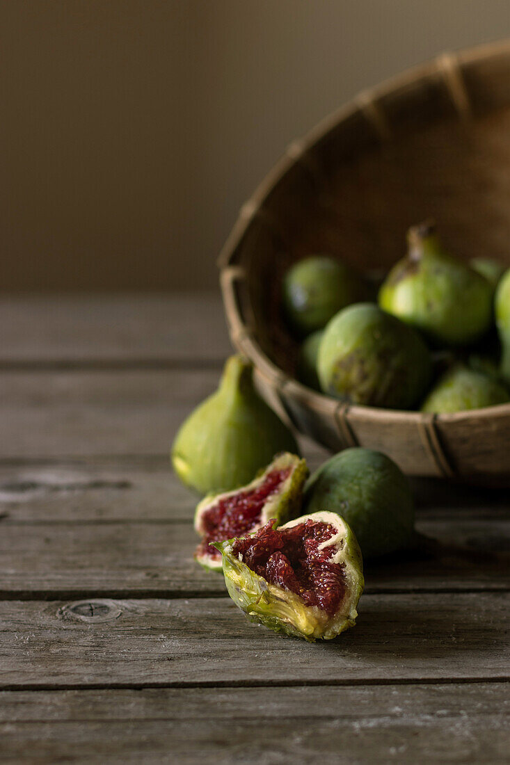 Nahaufnahme eines Korbes mit grünen Feigen und geteilten Früchten mit rotem Fruchtfleisch auf einem Tisch