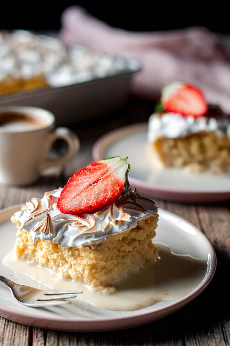 Süßes köstliches Stück Dreimilchkuchen mit einer halben frischen Erdbeere auf einem weißen Teller auf einem Holztisch