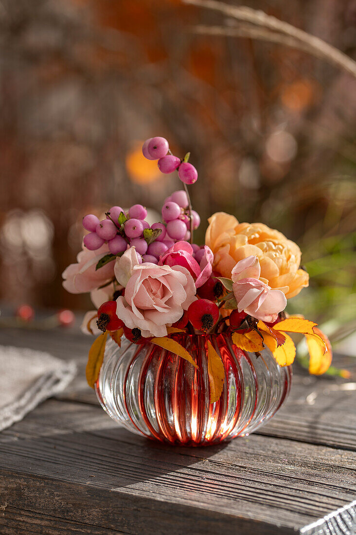 Bouquet of roses (Rosa) and snowberry (Symphoricarpos) 'Amethyst' in vase on garden bench