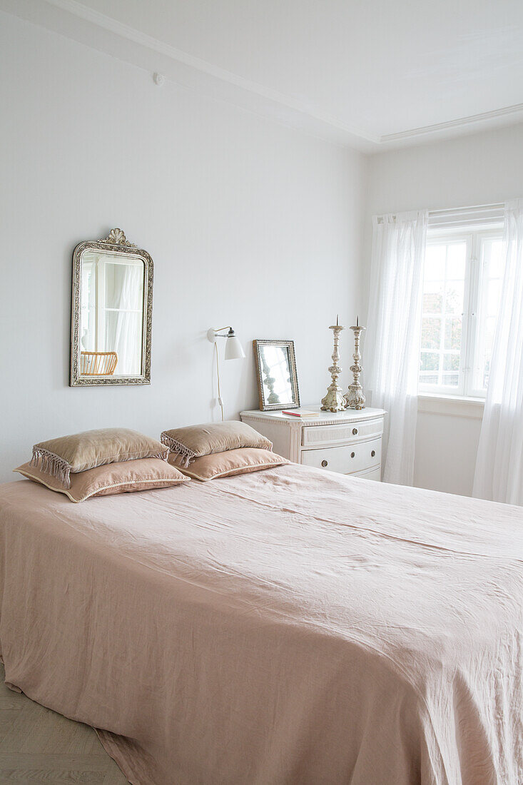 Bed with rose-colored bedspread, antique mirror and candlesticks in bedroom