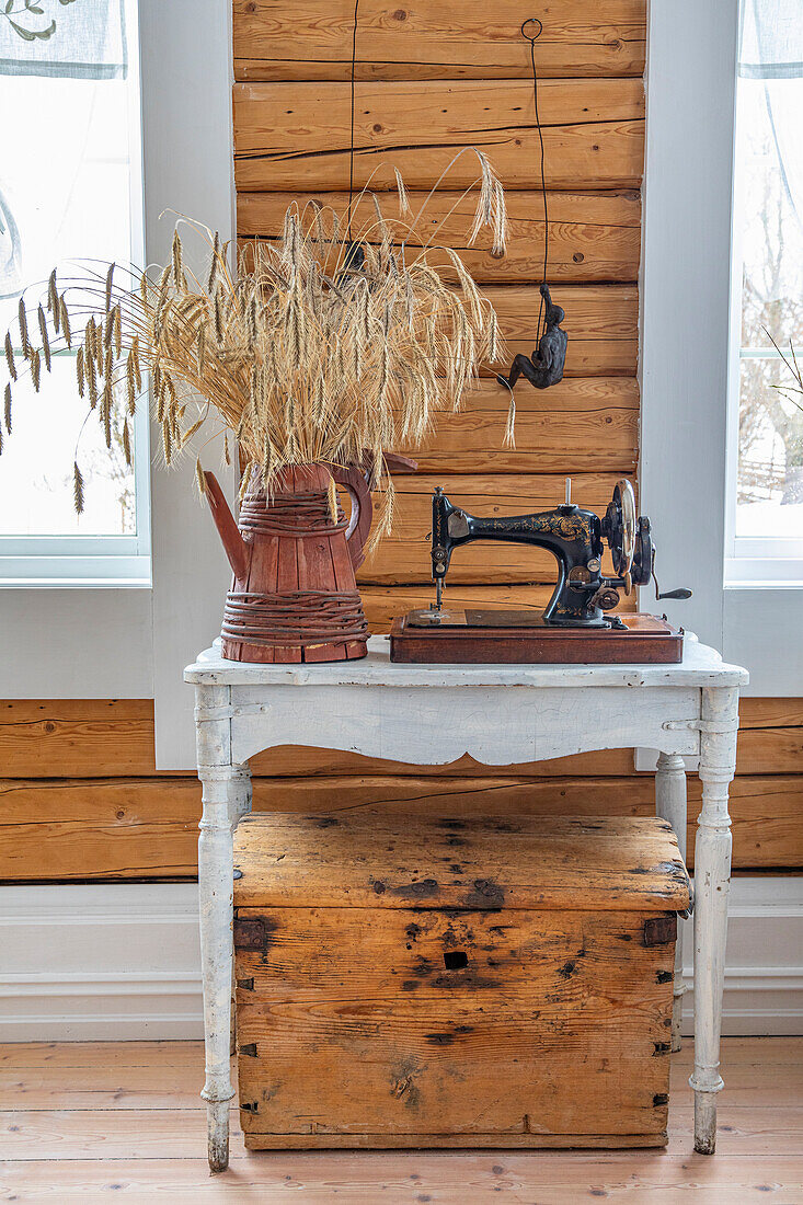 Old table with sewing machine and jug as vase in front of wall with wooden panelling