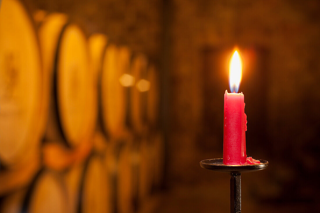 A burning red candle in a wine cellar