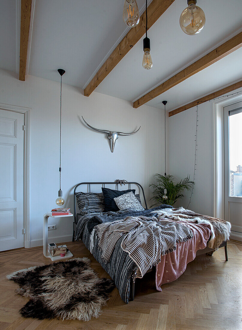 Bedroom with wooden beamed ceiling, metal bed frame and herringbone parquet flooring