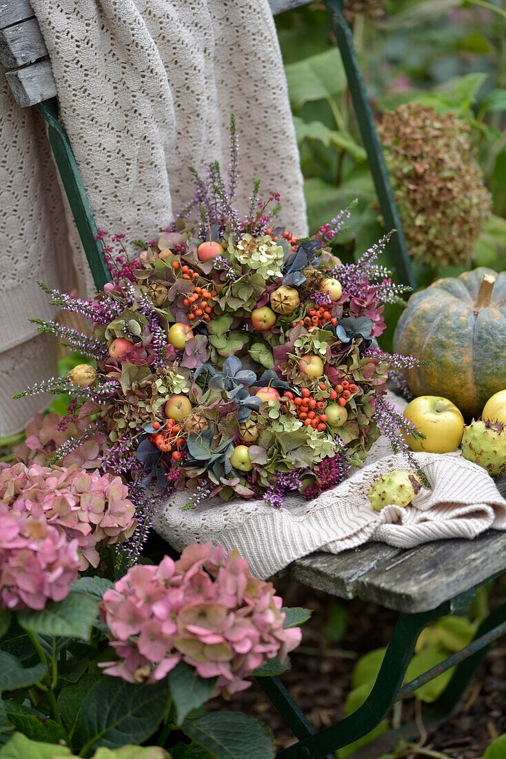 Colourful autumn wreath of hydrangeas, seed pods, heather, ornamental apples and rowan berries on a rustic garden chair