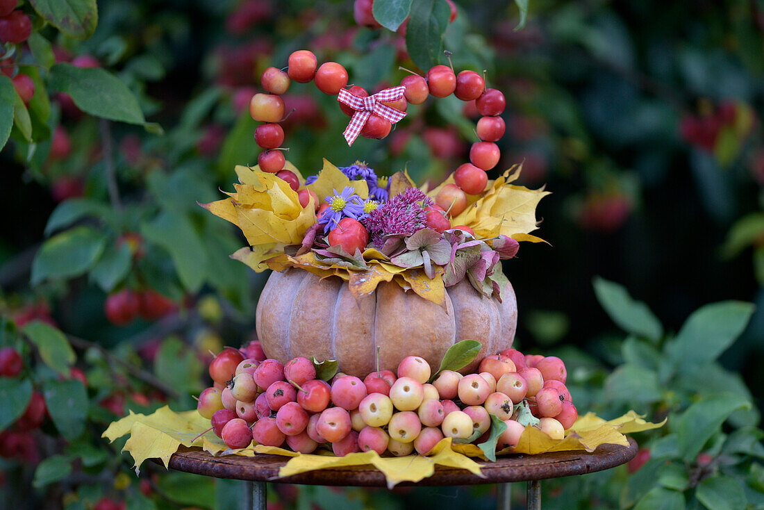 Autumn decoration made from pumpkin, ornamental apples and leaves with a heart shape made from apples